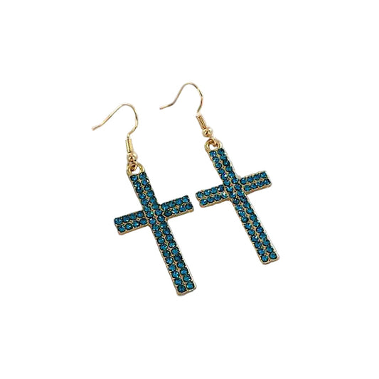 Cross-shaped earrings with blue gemstones on a white hexagonal stand against a beige background